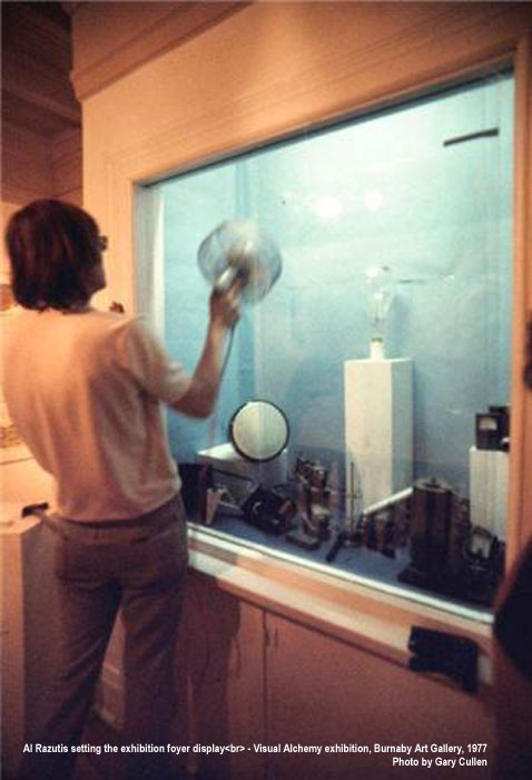 Al Razutis setting the exhibition foyer display with archaic tech items  for Visual Alchemy exhibition, Burnaby Art Gallery, 1977